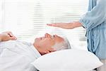 Massage therapist performing Reiki over senior man at health spa