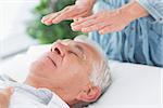 Massage therapist performing Reiki over senior man at health spa