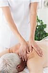 Female massage therapist massaging back of senior man in clinic