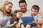 Family of four using digital tablet together on sofa at home