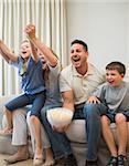 Excited family screaming while watching television on sofa at home