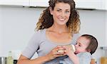 Portrait of attractive woman feeding milk to baby from bottle in kitchen