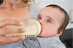 Mother feeding milk to baby boy from bottle at home