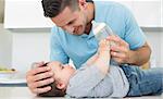 Caring father feeding milk to baby boy at kitchen counter