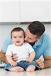 Loving father kissing baby boy sitting on kitchen counter