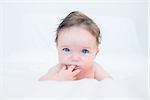 Portrait of cute baby with finger in mouth lying on bed