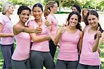 Portrait of happy female breast cancer participants gesturing thumbs up during campaign at park