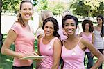 Portrait of confident female volunteer and participants at breast cancer campaign in park