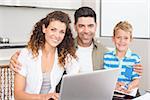 Happy little boy using laptop with parents at table at home in kitchen