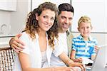 Cute little boy using laptop with parents at table at home in kitchen