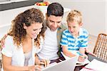 Cute little boy using laptop with his parents at table at home in kitchen