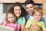 Happy family sitting on sofa with laptop at home in living room