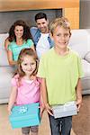 Siblings holding presents in front of parents on the couch at home in living room
