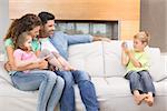 Little boy taking photo of family on the sofa at home in living room