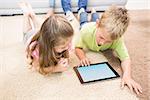 Smiling siblings lying on the rug using a tablet at home in living room