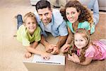 Happy siblings lying on the rug using laptop with their parents at home in living room
