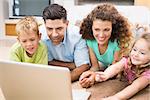 Cute siblings lying on the rug using laptop with their parents at home in living room