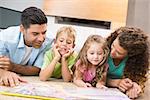 Cute siblings lying on the rug reading storybook with their parents at home in living room