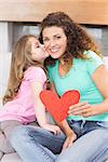 Smiling mother getting a heart card and a kiss from her daughter at home in living room