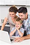 Parents using laptop with their son at home in kitchen