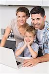 Smiling parents using laptop with their son at home in kitchen