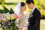 Close-up of bouquet with blurred newlywed couple in background at the park