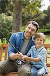 Smiling father and son fishing while sitting on park bench