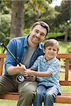 Portrait of a smiling father and son fishing while sitting on park bench