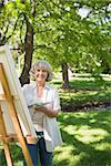 Portrait of a smiling mature woman painting on canvas in the park