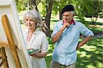 Man watching mature woman paint on canvas in the park