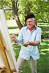 Happy mature man painting on canvas in the park