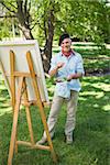 Full length portrait of a mature man painting on canvas in the park