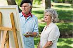 Woman watching mature man paint on canvas in the park