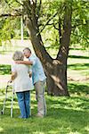 Rear view of a mature man assisting woman with walker at the park
