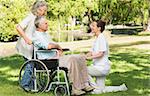 Two women with a mature man sitting in wheel chair at the park