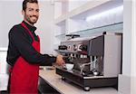 Smiling young barista making cup of coffee in a cafe