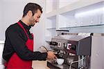 Happy attractive barista making cup of coffee in a cafe