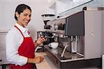 Pretty barista making coffee smiling at camera in a cafe