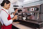 Pretty barista steaming jug of milk at coffee machine in a cafe