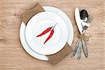 Red chili peppers on plate and silverware set on wooden table