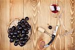 Red wine glass, corkscrew and grape on wooden table background