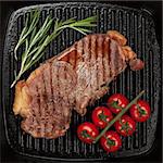 Sirloin steak with rosemary and cherry tomatoes on frying pan closeup