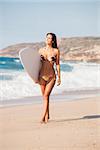 A beautiful surfer girl walking at the beach with her surfboard