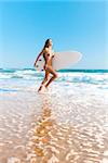 A beautiful surfer girl running at the beach with her surfboard