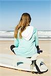 Teenage surfer girl sitting in the beach and checking the waves