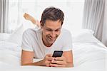 Happy casual young man text messaging in bed at home