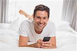 Portrait of a happy casual young man text messaging in bed at home