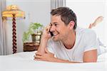 Casual relaxed young man using mobile phone in bed at home