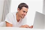Relaxed casual young man using laptop in bed at home