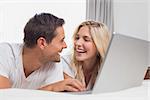 Cheerful relaxed casual young couple using laptop in bed at home